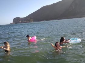 A lively group enjoys a fun day swimming in the ocean with colorful floaties, surrounded by stunning coastal scenery.