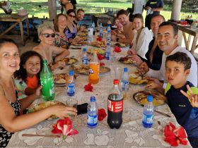 A joyful group gathers around a table enjoying a delicious meal together, perfect for family celebrations or group outings in a tropical setting.