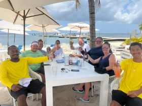 A lively group enjoys drinks at a beachside table, celebrating together in a picturesque setting — perfect for memorable gatherings and fun in the sun.