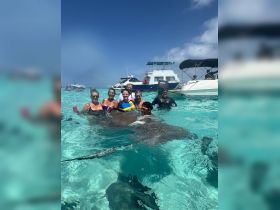 A group of excited guests interacts with stingrays in crystal-clear waters, creating unforgettable memories during their aquatic adventure.