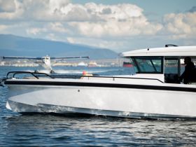 A sleek speedboat navigates the water with a pilot at the helm, showcasing its elegant design against a backdrop of mountains and clouds.