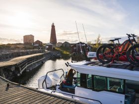 A scenic view of a lighthouse and charming buildings, with a boat docked nearby and bicycles on the roof, perfect for exploring the coastal landscape.