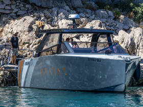 A sleek boat named 'AFITAT' is docked near rocky shores, with people visible on the deck and nearby, showcasing a vibrant day on the water.