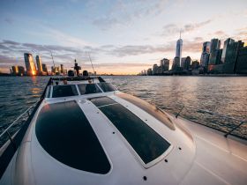 A stunning sunset view from a boat cruising past the iconic New York City skyline, showcasing the vibrant reflections on the water and the excitement of urban boating adventures.