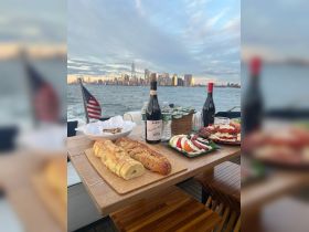 A beautifully arranged spread of gourmet food and wine on a boat, with a stunning city skyline in the background — perfect for a luxurious dining experience on the water.