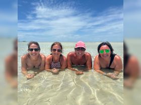 A joyful group of friends enjoys a sunny day at the beach, relaxing in shallow waters — perfect for memorable summer outings and beach adventures.