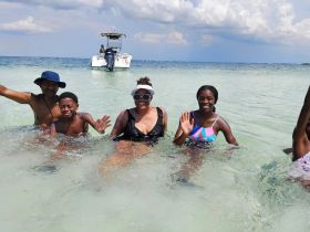 A joyful family enjoys a fun day at the beach, swimming in shallow waters with a boat anchored nearby — perfect for memorable summer adventures.