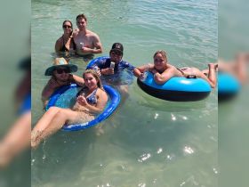 A lively group enjoys a fun day in the water, floating on inflatable rings and sipping drinks — the perfect way to celebrate summer with friends.