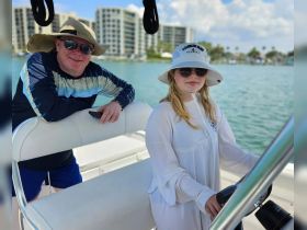 A father and daughter enjoy a day on the water, with the daughter at the helm of the boat, showcasing a fun family outing.