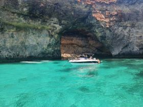 A boat is anchored near a stunning cave, surrounded by crystal-clear turquoise waters, perfect for exploring and enjoying the natural beauty of the coastline.