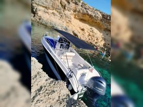 A boat is anchored near a rocky shore with people enjoying the water, creating a perfect scene for a summer adventure.