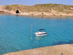 A speedboat navigates through crystal-clear waters near a rocky coastline, showcasing the beauty of a serene marine landscape.