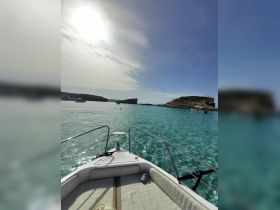 A stunning view from the bow of a boat, showcasing crystal-clear waters and nearby islands, with swimmers enjoying the sun — a perfect day on the water.