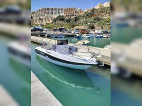 A sleek speedboat docked in a picturesque marina, showcasing its design against a backdrop of coastal buildings and clear waters.