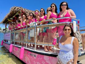 A lively group of women in pink swimsuits celebrates on a vibrant party boat, perfect for bachelorette parties or summer fun on the water.