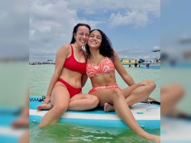Two friends share a joyful moment while paddleboarding in shallow waters, showcasing the fun and excitement of summer water activities.