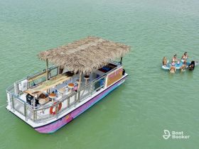 A lively group enjoys a fun day on the water, paddleboarding and socializing around a tiki boat — perfect for summer parties and water adventures.