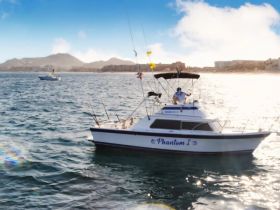 The 'Phantom I' fishing boat is seen cruising through the sparkling waters, showcasing its sleek design against a scenic backdrop of mountains and coastline.