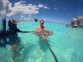 A woman joyfully interacts with a stingray in crystal-clear waters, showcasing a unique wildlife experience in a tropical paradise.