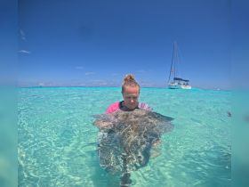A woman interacts with a stingray in shallow turquoise waters, showcasing a unique wildlife experience in a tropical paradise.