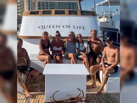 A lively group poses for a photo aboard the 'Queen of Life' boat, capturing a moment of fun and camaraderie on the water.
