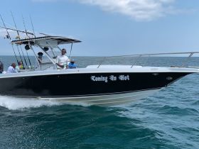 A fishing boat named 'Coming In Hot' speeds through the water with a group of anglers onboard, showcasing the thrill of a day out on the ocean.