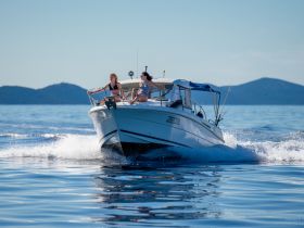 Two friends enjoy a thrilling ride on a boat, cutting through the calm waters with stunning mountain scenery in the background — a perfect day for adventure on the sea.