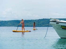 Two women enjoy paddleboarding in calm waters, showcasing a perfect summer day on the water — ideal for outdoor adventures and fun activities.