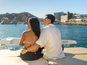 A couple enjoys a romantic moment on a boat, basking in the sunshine and taking in the beautiful waterfront views — perfect for a getaway or special occasion.