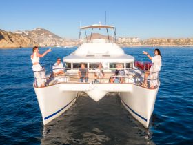 A lively group enjoys drinks aboard a catamaran, celebrating with stunning coastal views — perfect for memorable outings and gatherings on the water.