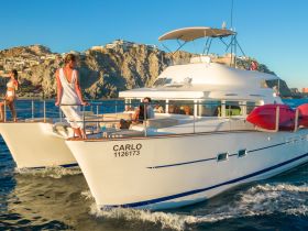 A lively group enjoys their time aboard a catamaran, with stunning coastal views in the background — perfect for celebrations and group outings on the water.
