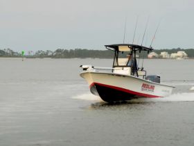 A sleek speedboat named 'Redline' cruises through calm waters, showcasing its design and performance. Perfect for fishing or leisure outings.
