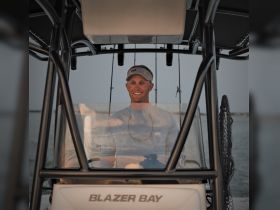 A smiling captain at the helm of a Blazer Bay boat, showcasing the interior console and a perfect setting for a day on the water.