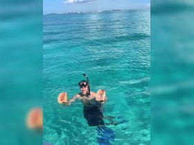A snorkeler proudly displays two conch shells while swimming in the crystal-clear waters, showcasing the vibrant marine life experience in the Bahamas.