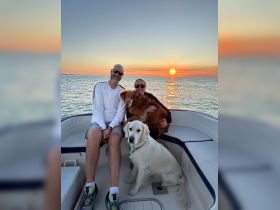 A couple enjoys a beautiful sunset on their boat, accompanied by their two dogs — a perfect moment for pet lovers and sunset enthusiasts.
