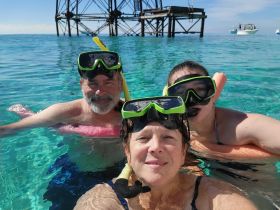 A joyful group enjoys snorkeling in crystal-clear waters, capturing a fun moment together with a backdrop of a submerged structure.