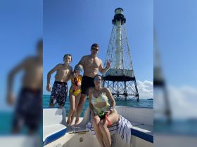 A joyful family poses for a photo on their boat with a lighthouse in the background, ready for a day of snorkeling and fun in the sun.