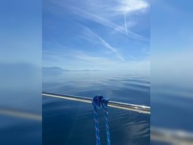 A close-up shot of a blue rope tied on a boat railing with a serene water background, showcasing a peaceful day at sea.