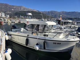 A sleek boat docked in a marina, showcasing its clean lines and modern design against a picturesque backdrop of mountains and clear skies.
