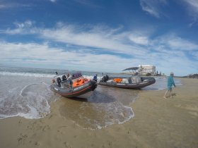Two boats are beached on a sandy shore, with a person walking nearby — a perfect scene for beach adventures and water activities.