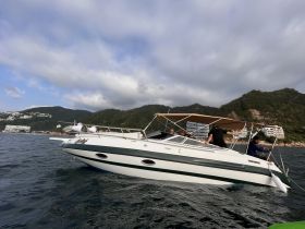 A lively group enjoys a day on the water aboard a speedboat, with fishing gear visible and stunning coastal scenery in the background.