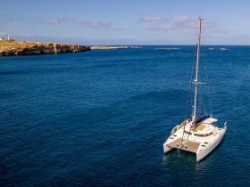 A stunning aerial view of a catamaran anchored in serene blue waters, showcasing the beauty of sailing and the tranquility of the open sea.