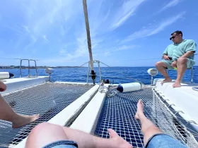 Two friends relax on the deck of a catamaran, enjoying the ocean view and sunny skies — a perfect moment for leisure on the water.
