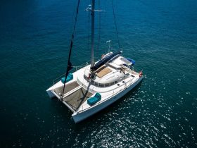 A stunning aerial view of a catamaran sailing through crystal-clear waters, showcasing its sleek design and inviting deck space.