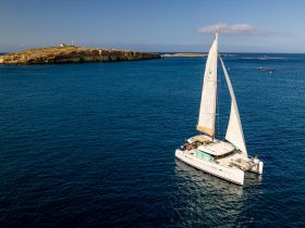 A stunning aerial view of a catamaran sailing in clear blue waters, with a picturesque island in the background, perfect for showcasing sailing adventures.