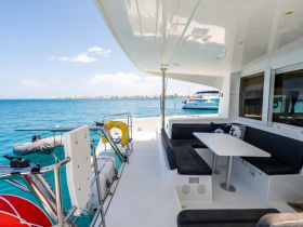 Interior view of a spacious lounge area on a catamaran, featuring comfortable seating and a dining table, perfect for relaxing while enjoying the ocean views.