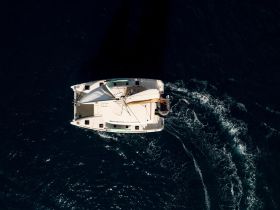 Aerial view of a catamaran sailing through deep blue waters, showcasing its sleek design and vibrant sails — perfect for adventure seekers and sailing enthusiasts.