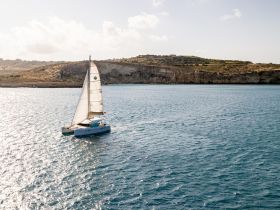 A stunning aerial view of a catamaran sailing through tranquil waters, surrounded by picturesque cliffs — perfect for exploring coastal landscapes.