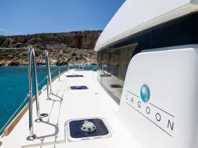 A stunning view of a Lagoon yacht's deck, showcasing its sleek design against a backdrop of turquoise waters and rocky cliffs — perfect for luxury sailing adventures.