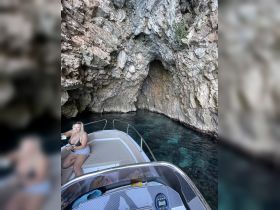 A woman enjoys a moment on a boat while exploring a stunning rocky cave, showcasing the beauty of nature and adventure on the water.